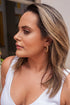 A woman with highlighted brown hair wears a textured gold hoop earring while wearing a white top.
