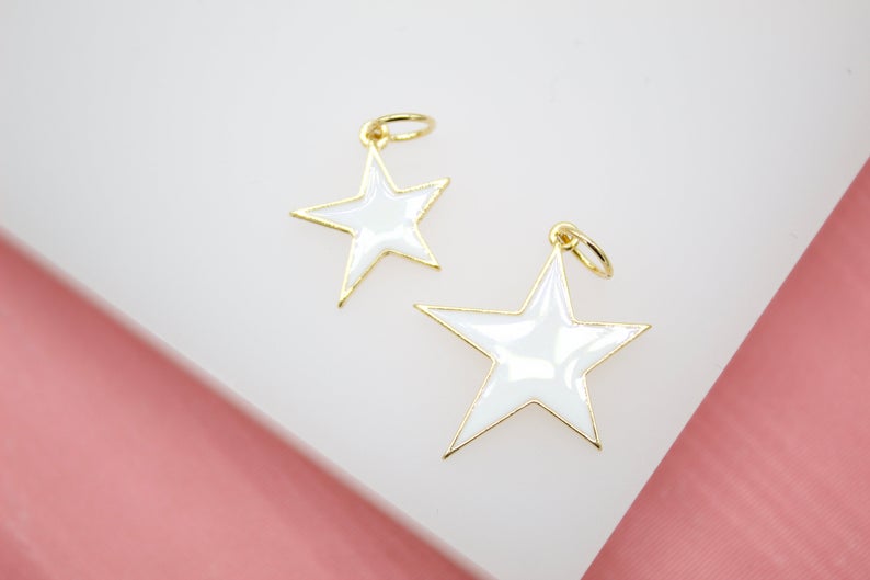 Two gold-rimmed white star charms rest on a white display surface against a pink background.