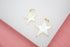 Two gold-rimmed white star charms rest on a white display surface against a pink background.