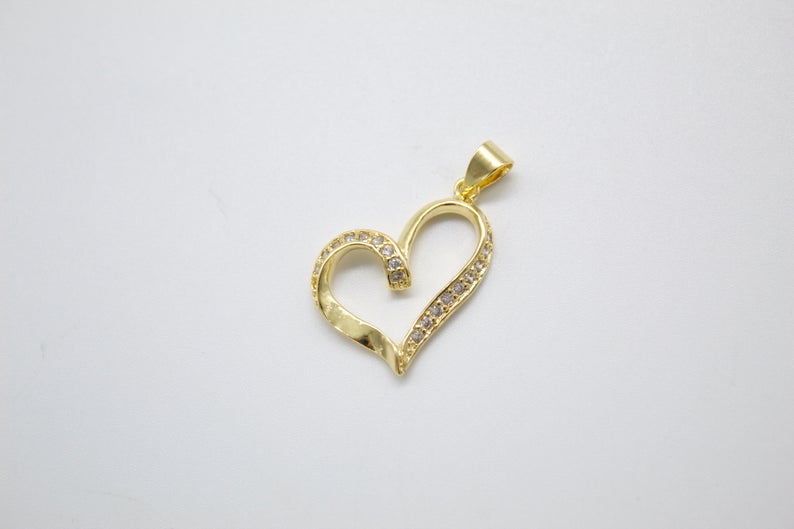 A gold heart-shaped pendant sparkles with embedded cubic zirconia stones against a neutral white background.