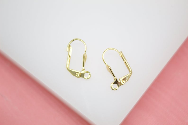 A pair of shiny gold-plated leverback earring findings rests on a white display surface.