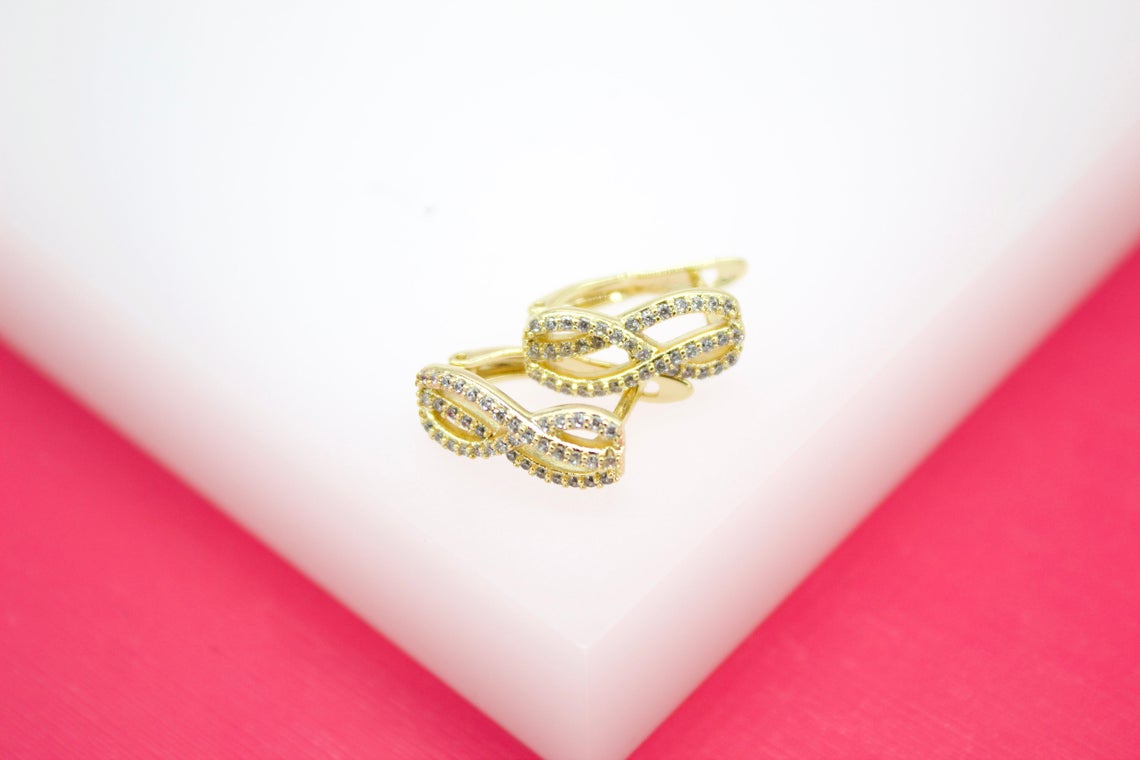 A pair of gold infinity-shaped hoop earrings encrusted with sparkling CZ stones rests on a white display surface.