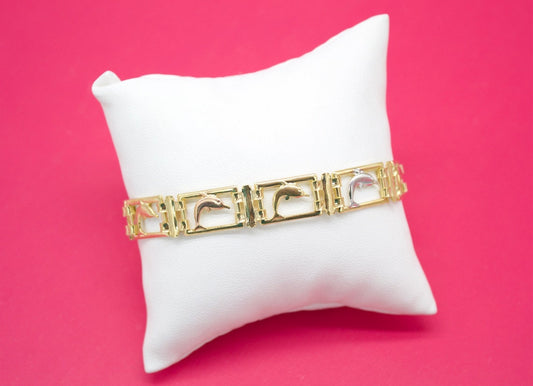 A gold and silver dolphin link bracelet rests elegantly on a white display pillow against a vibrant pink background.