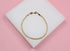 A delicate gold curb chain bracelet rests on a white display block against a soft pink background.