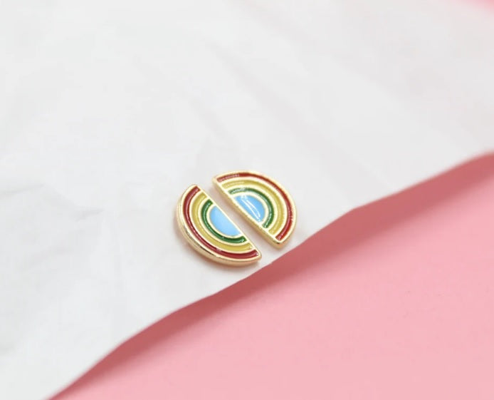 Two gold-rimmed enamel rainbow earrings rest on a white and pink background.
