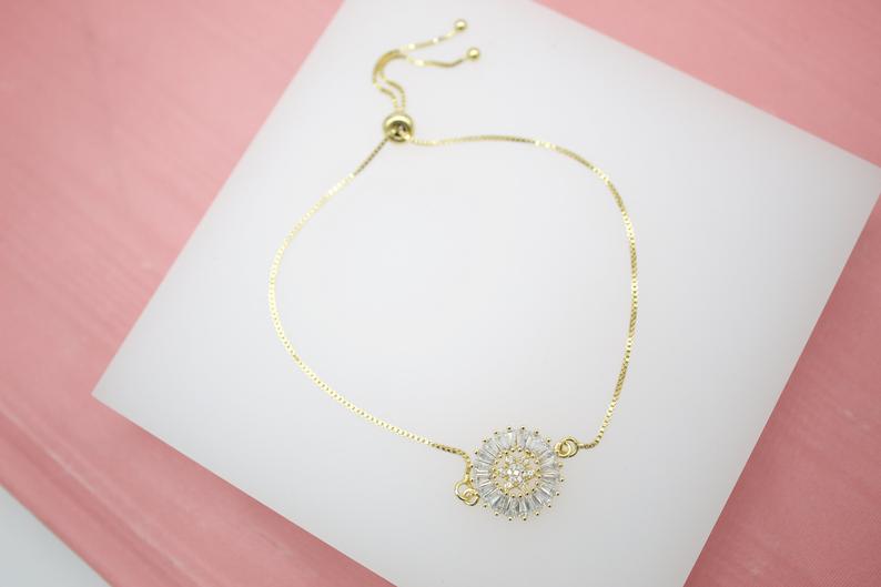 A delicate gold slider bracelet displays a sparkling cubic zirconia sunburst charm on a white display pad.
