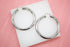 A pair of polished silver hoop earrings rests on a white display block against a textured pink background.