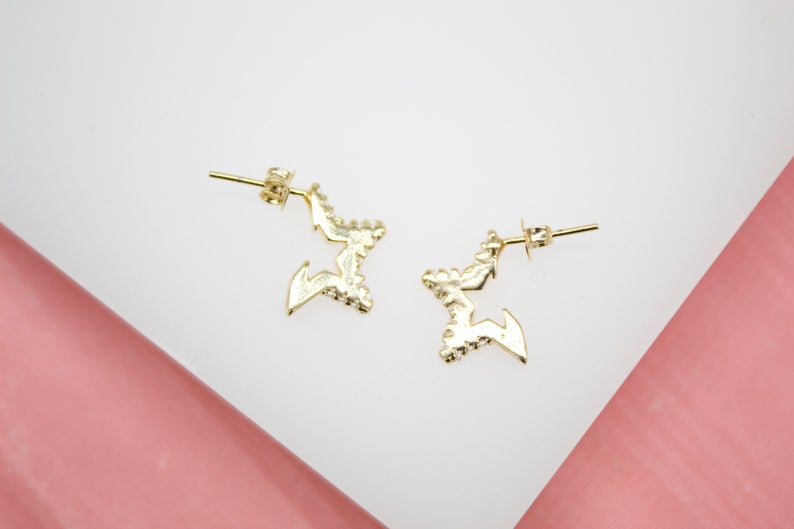 A pair of gold star stud earrings rests against a white and pink surface.