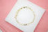 A delicate gold link bracelet rests on a white display surface against a pink background.
