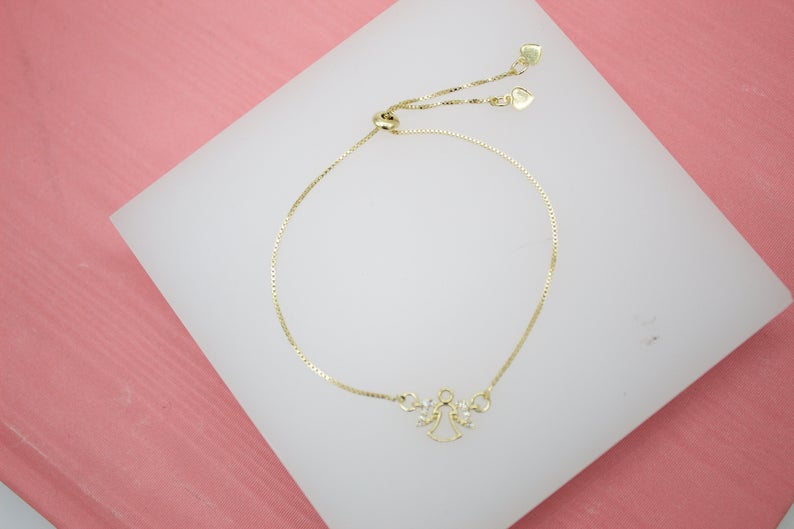 A delicate gold adjustable bracelet features a sparkling angel pendant centered on a white display surface.
