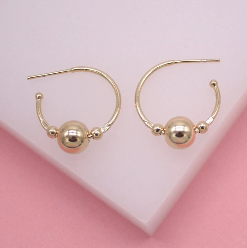 A pair of gold hoop earrings featuring a central bead rests on a white and pink display surface.