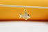 A gold fish pendant with sparkling cubic zirconia stones hangs delicately from a wooden stick against a bright orange and white backdrop.