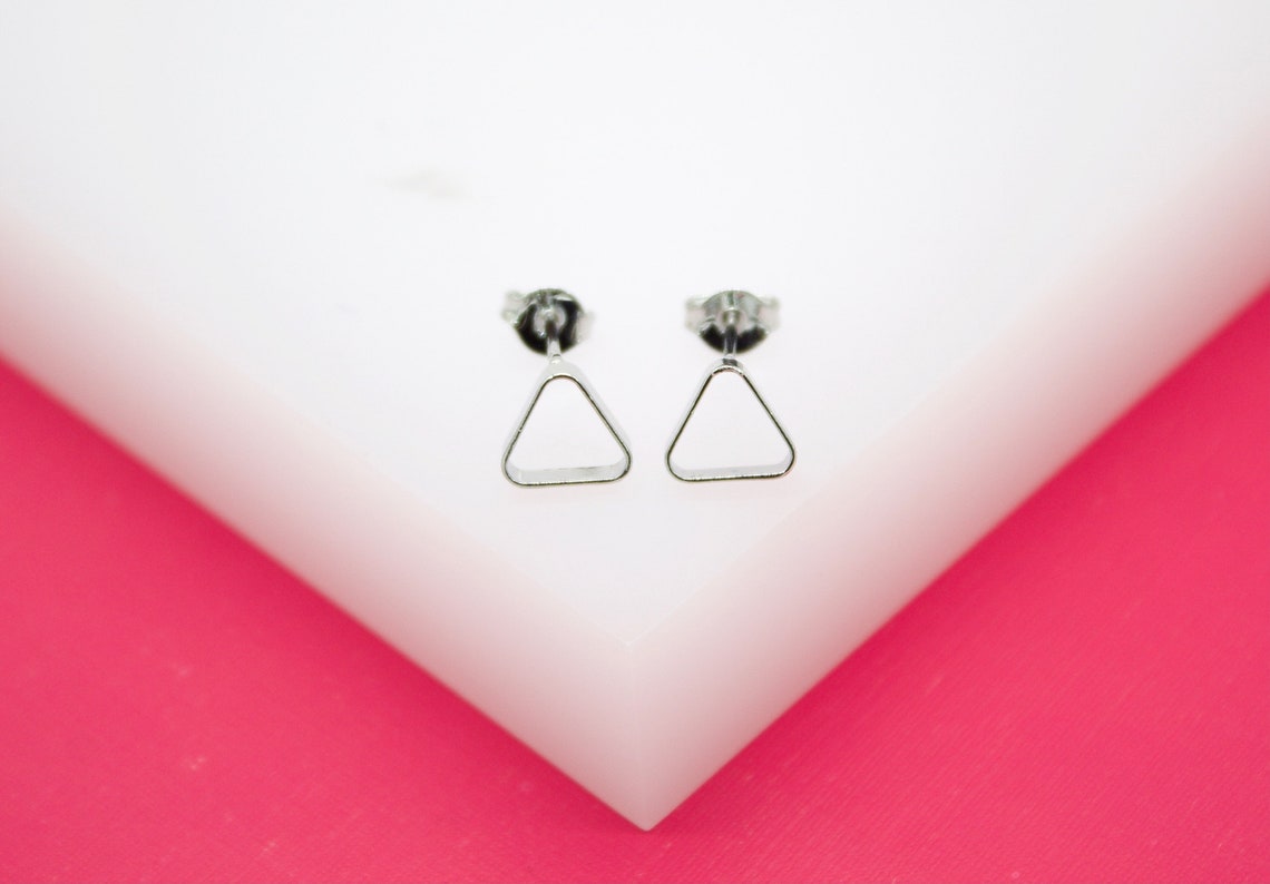 A pair of silver geometric triangle stud earrings rests neatly on a white and pink display stand.