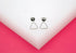 A pair of silver geometric triangle stud earrings rests neatly on a white and pink display stand.