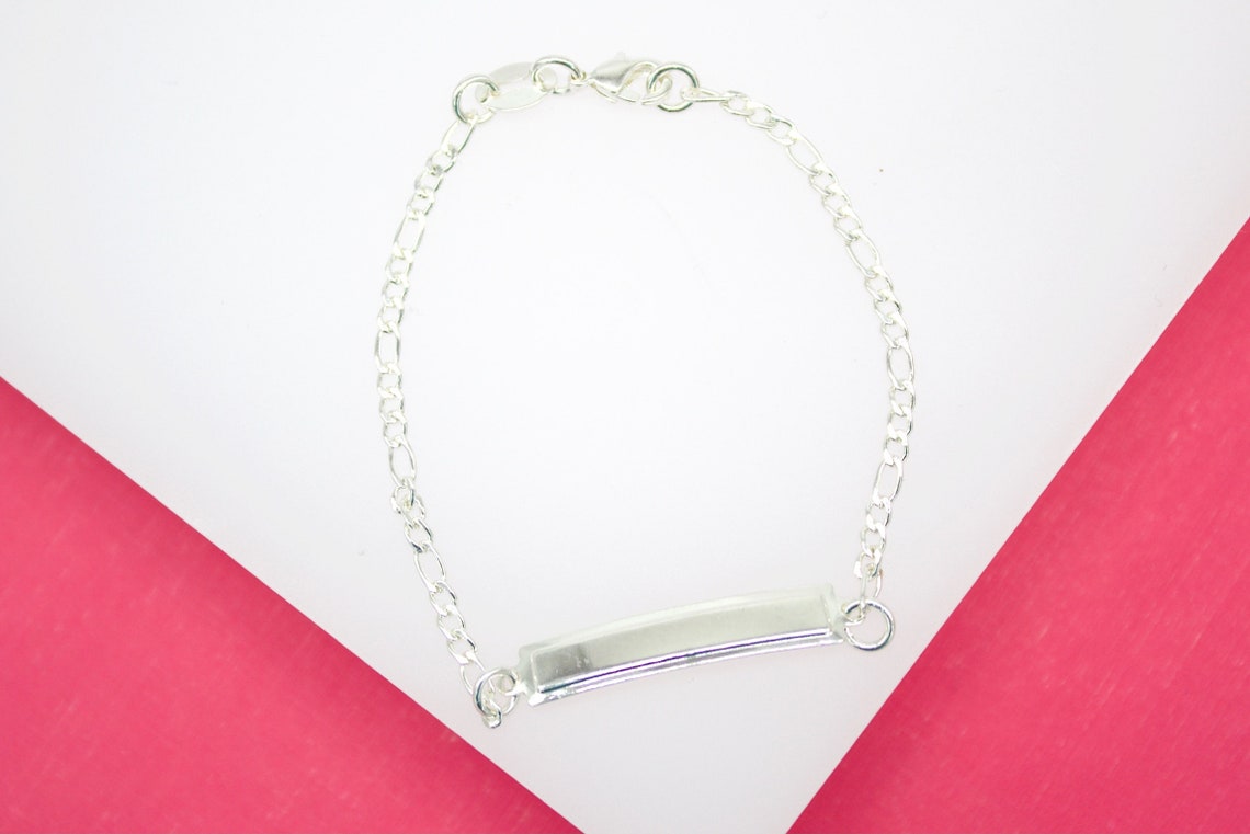 A sterling silver ID bar bracelet rests on a white and pink surface.