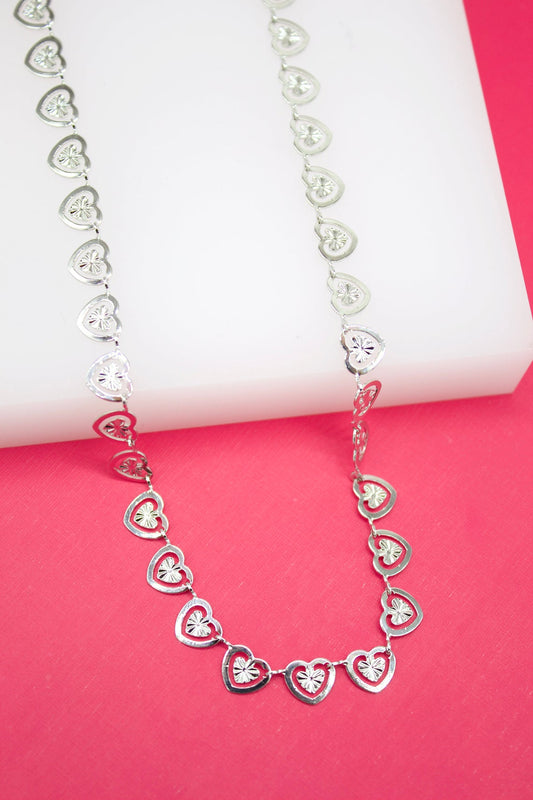 A delicate white gold heart link necklace rests against a vibrant pink and white background.