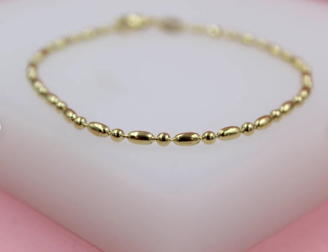 A delicate gold bead bracelet rests gracefully on a white display surface.