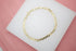 A delicate gold curb chain bracelet rests on a white display pad.