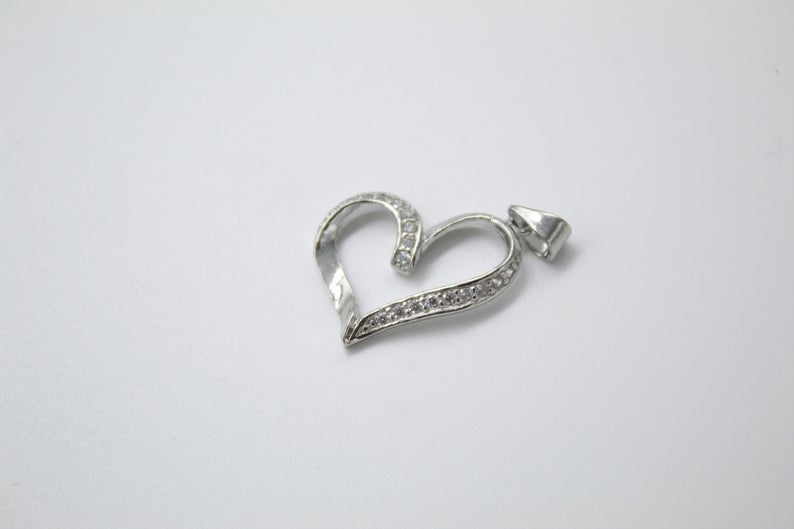 A silver heart-shaped pendant studded with small cubic zirconia stones rests against a plain white background.