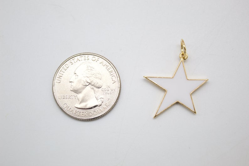 A white enamel star charm with gold trim rests beside a US quarter coin to show its scale.