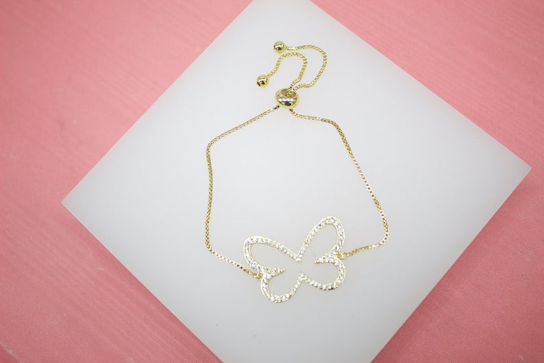 A delicate gold butterfly slider bracelet adorned with sparkling cubic zirconia stones rests on a white display surface.