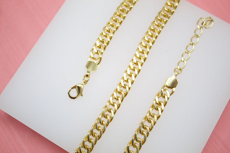 A gold-plated cuban link chain lies on a white surface against a pink background, showcasing its lobster clasp and adjustable extension.