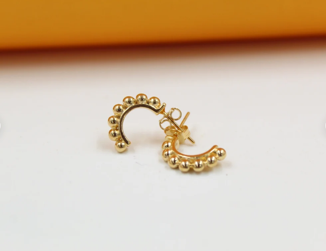 A pair of gold huggie hoop earrings featuring a beaded texture rests on a clean white surface.