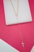 A delicate gold rosary necklace rests elegantly on a white display block against a vibrant pink background.