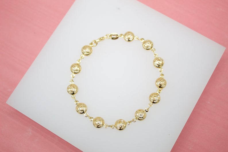 A gold chain bracelet featuring circular coin charms rests on a white display stand.