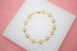 A gold chain bracelet featuring circular coin charms rests on a white display stand.