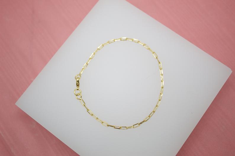 A delicate gold paperclip chain bracelet rests on a white display surface.