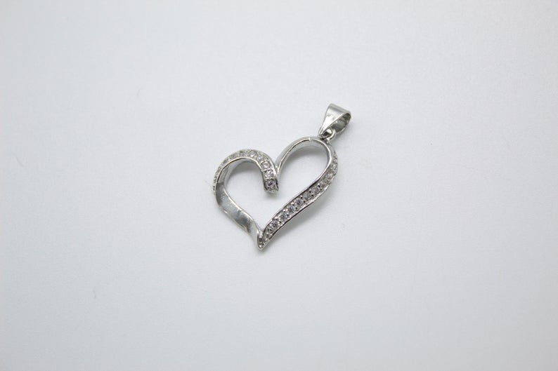 A sparkling diamond-encrusted silver heart pendant rests on a neutral background.