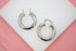A pair of thick, polished silver hoop earrings rests on a white and pink display surface.