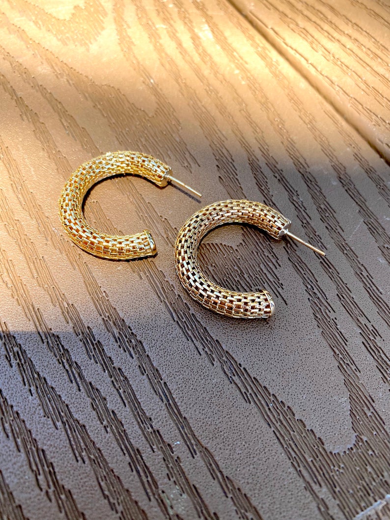 A pair of textured gold hoop earrings rests on a weathered wooden surface.