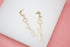 A pair of gold drop earrings spelling out the word "LOVE" with shimmering rhinestone embellishments rests on a white display surface.