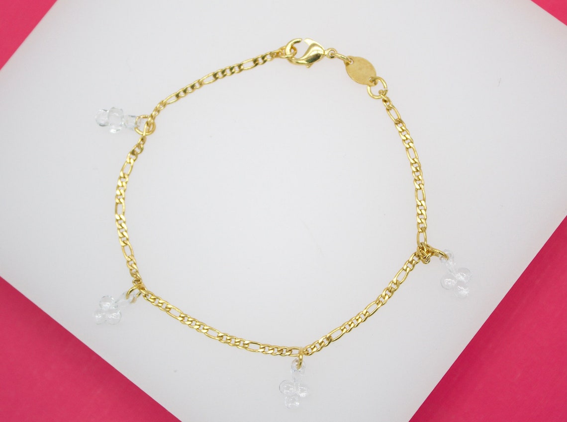 A gold chain bracelet features delicate clear glass flower charms dangling gracefully along its link.