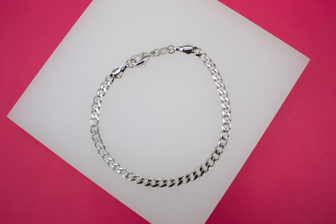 A polished silver curb chain bracelet rests on a white display card against a vibrant pink background.