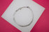 A polished silver curb chain bracelet rests on a white display card against a vibrant pink background.