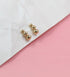 A pair of dainty gold ball cluster stud earrings rests on a crumpled white paper against a pink background.
