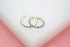 Two gold and silver rhinestone-encrusted ear cuffs rest on a white display surface against a soft pink background.
