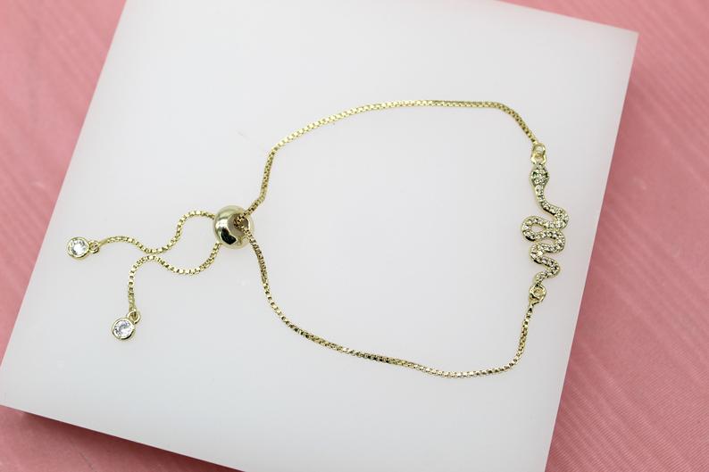 A gold snake slider bracelet with sparkling crystal accents rests on a white display surface.