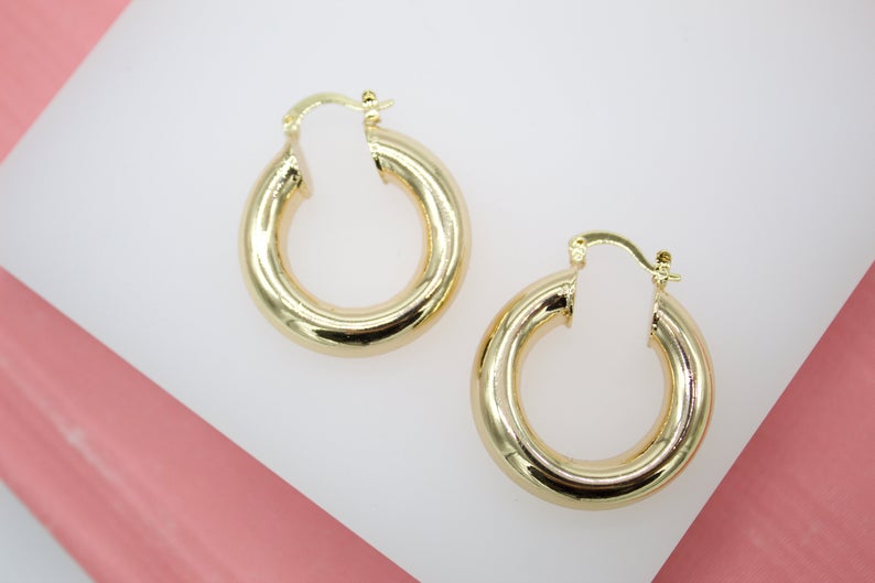 A pair of thick gold hoop earrings rests against a white and pink display surface.