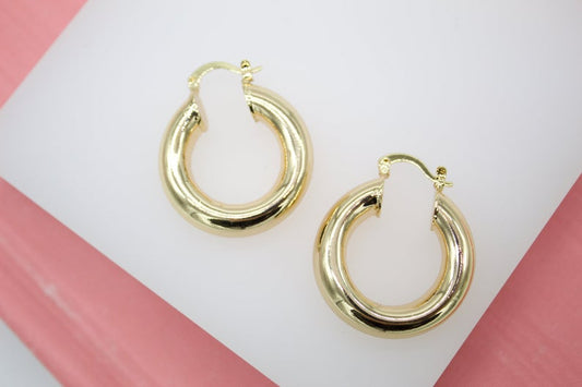 A pair of thick gold hoop earrings rests against a white and pink display surface.