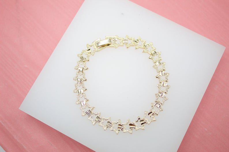 A delicate gold star-shaped link bracelet rests on a white display pad.