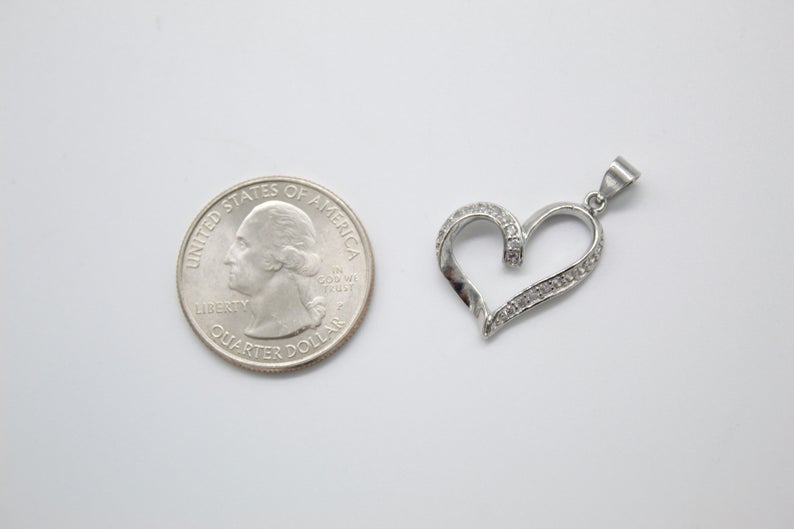 A sparkling diamond heart pendant rests next to a US quarter coin to showcase its size.