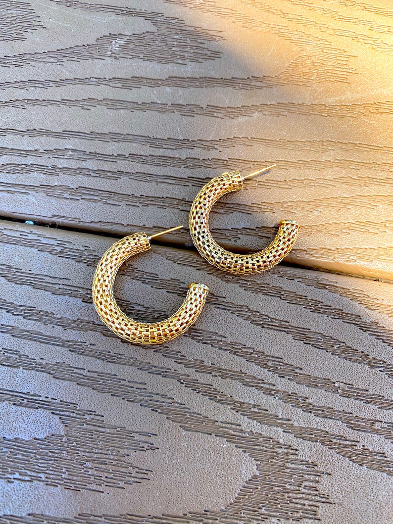 Two textured gold hoop earrings rest on a wooden surface in warm sunlight.