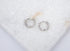 A pair of sparkling silver huggie hoop earrings rests delicately on a textured white marble surface.