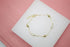 A delicate gold chain bracelet features alternating gold and pearl beads, resting on a white display surface.