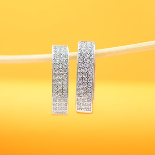 Two sparkling pave hoop earrings hang delicately from a thin twig against a vibrant yellow background.