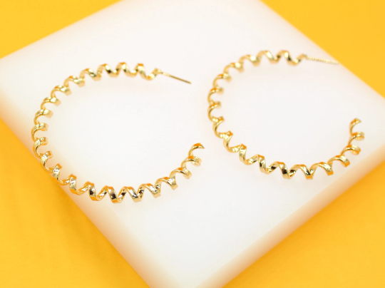 A pair of gold spiral hoop earrings rests on a white display block against a vibrant yellow background.